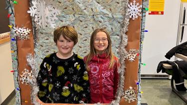 A smiling boy and girl inside a photo booth framed by snowflakes on a brown background