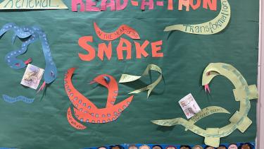 Coloured paper cutouts of snakes pasted onto a green paper background advertising an elementary school read-a-thon.