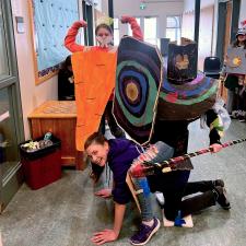 Three elementary school children posing in hallway wearing homemade gladiator costumes painted in bright colours.